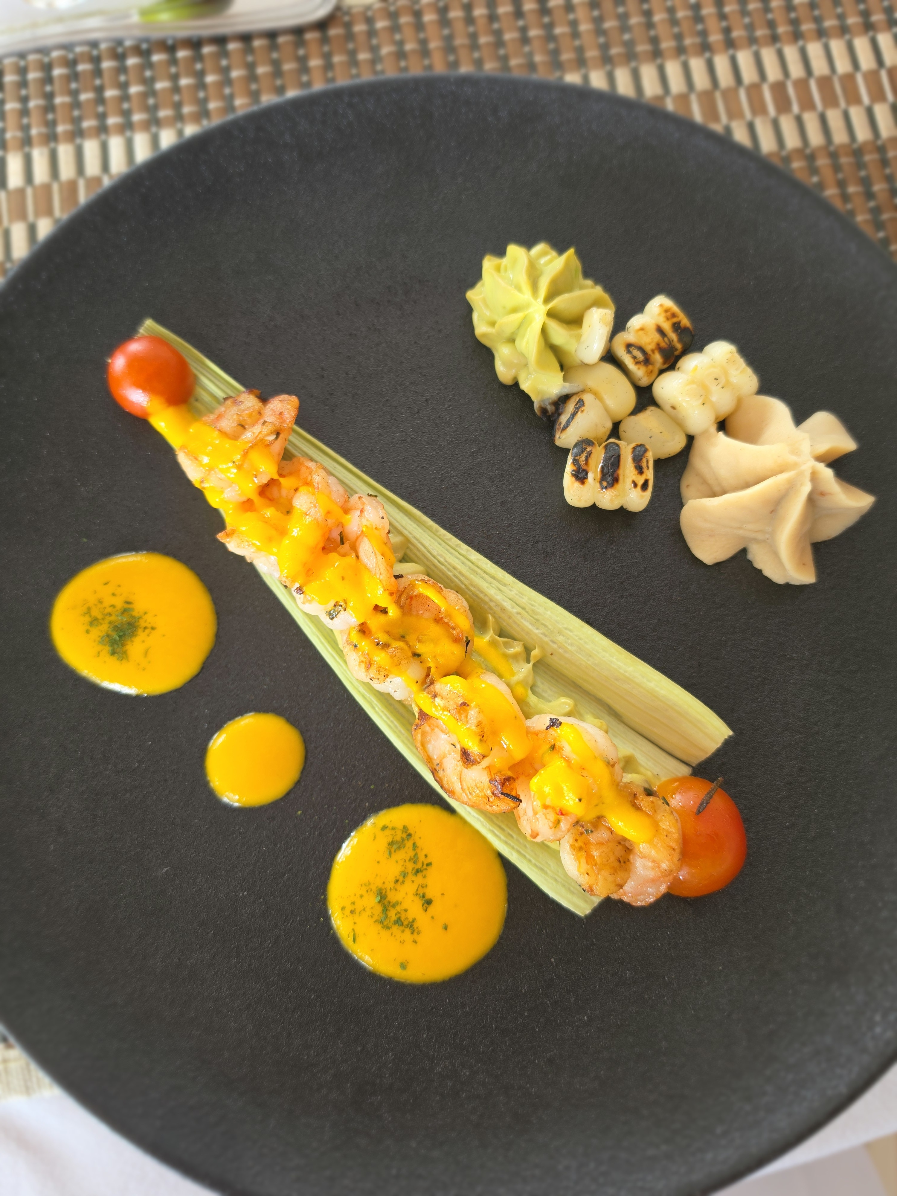 A prawn skewer plated with corn, heart of palm and a golden sauce