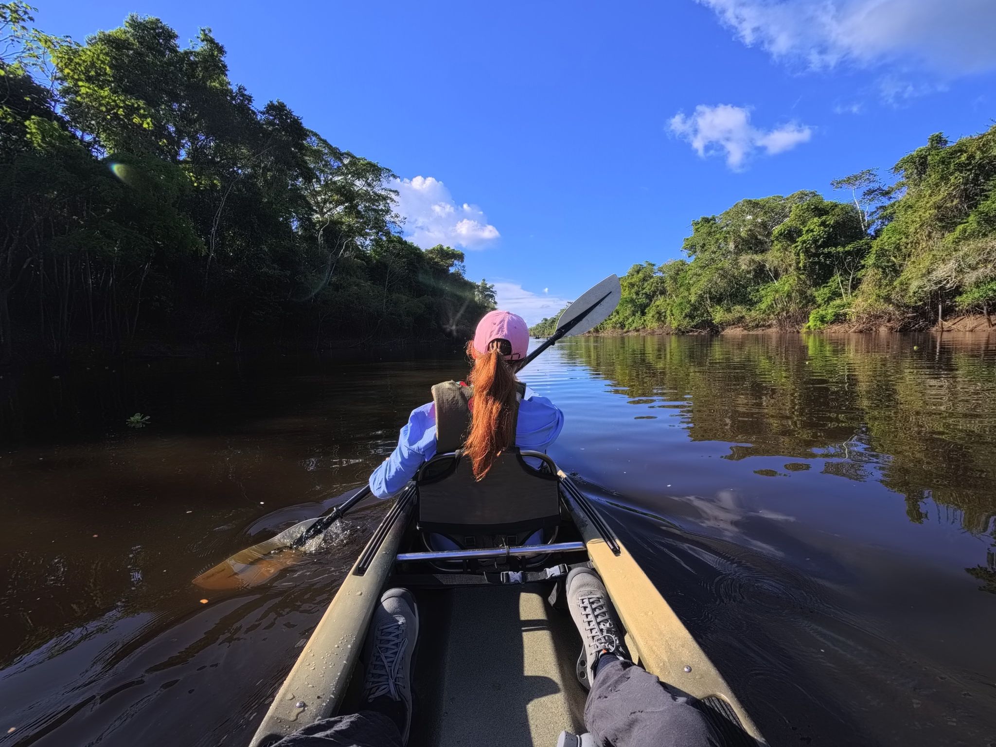 Kayaking along a narrow Amazon creek under a clear blue sky