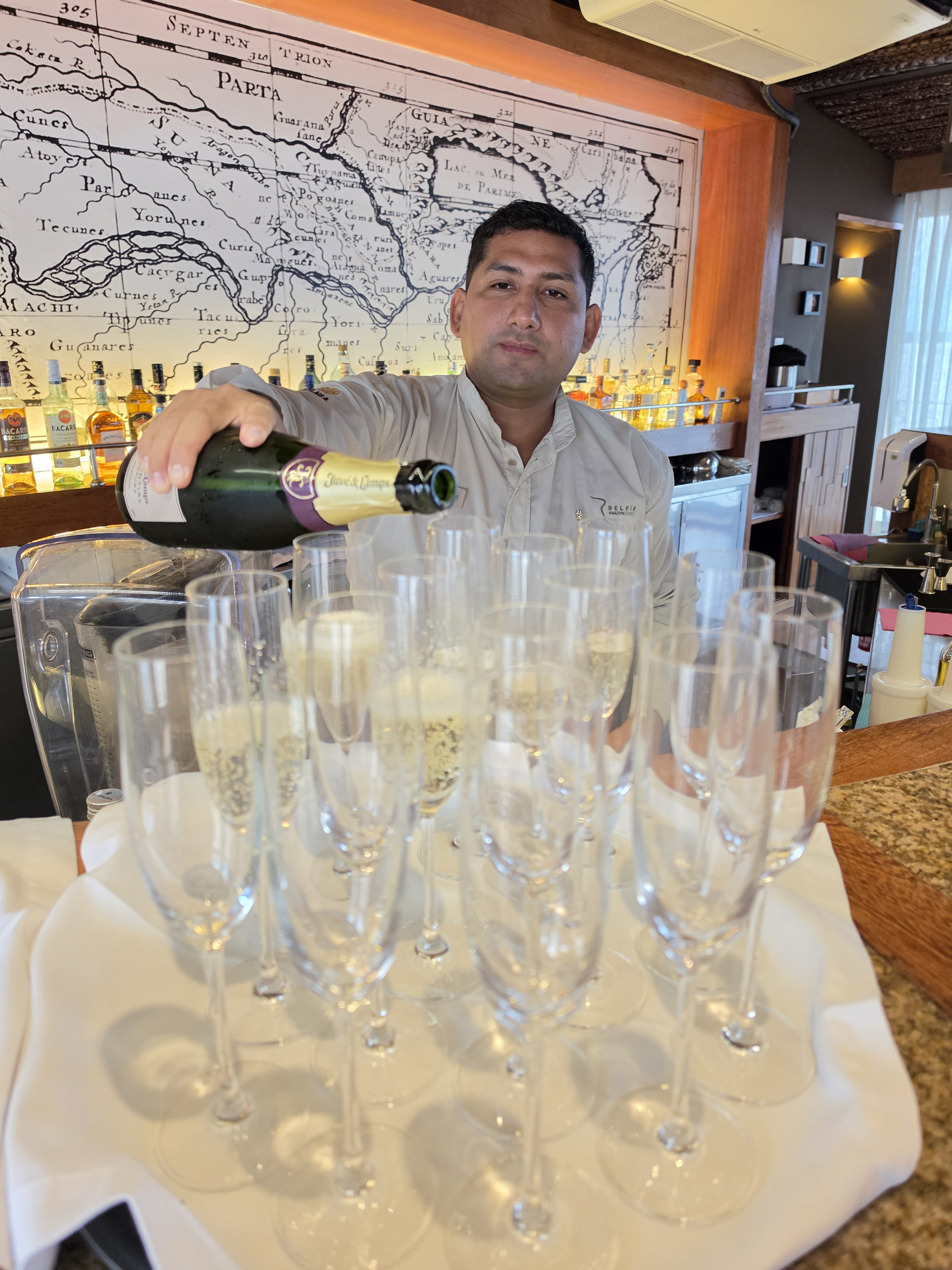 A Delfin barman pouring sparkling wine into a tray of glasses